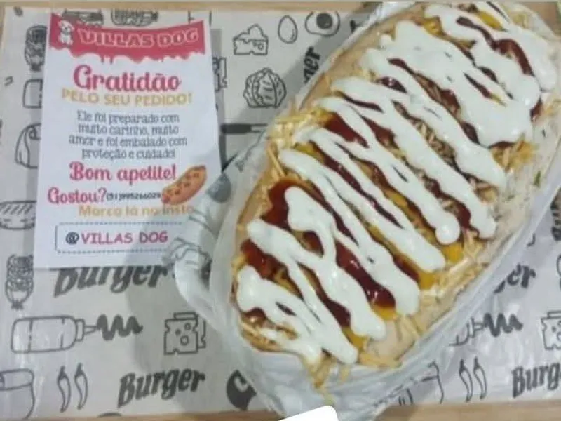Dog Aberto com molho e maionese da casa sobre o pão, ao lado do cartão de agradecimento do Villas Dog